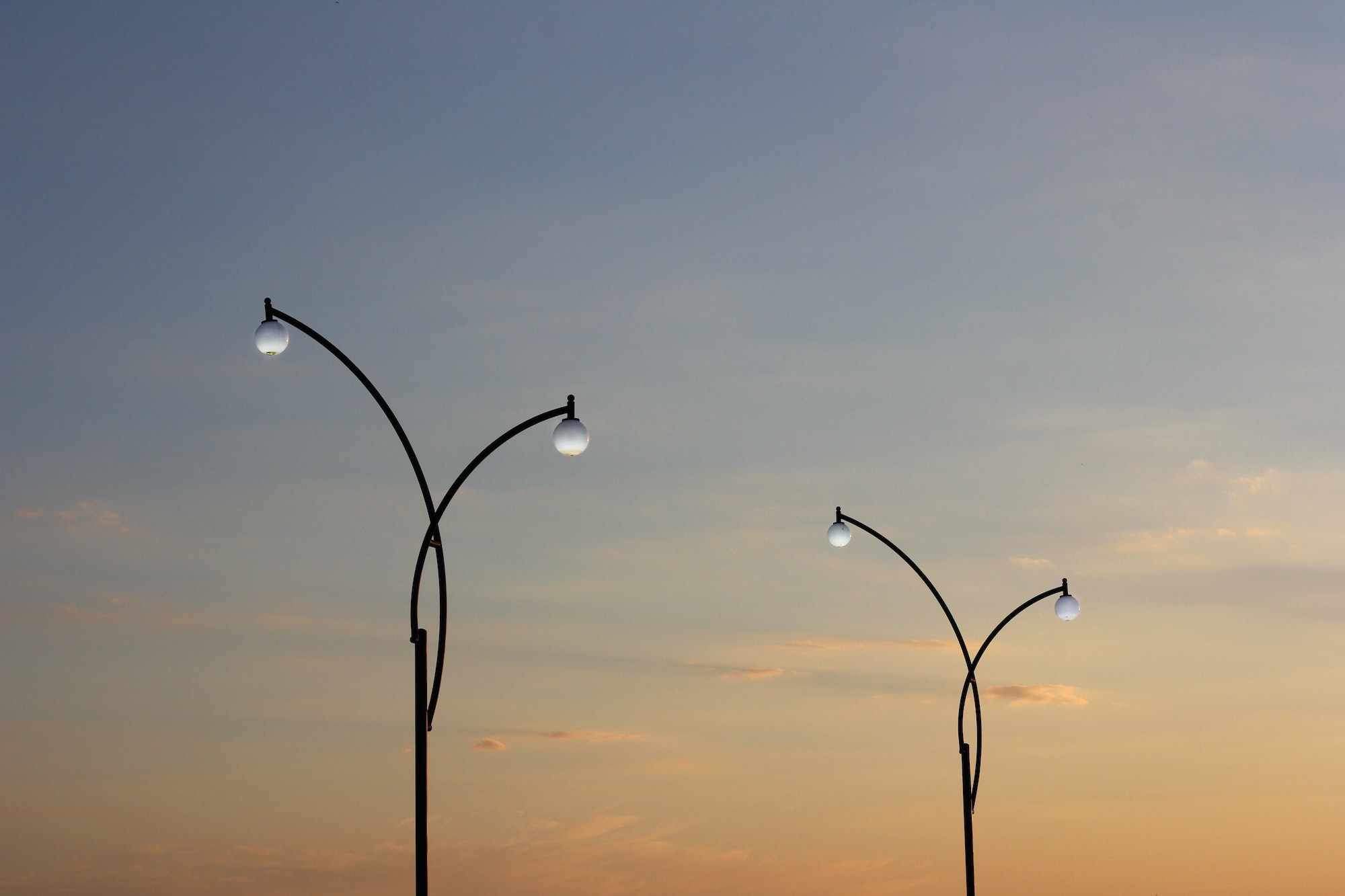 Two street lamp agains a sunset sky
